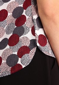 Blusa con una tela blanca con un patrón de lunares en rojo, rosa, gris y negro; textura suave; dobladillo curvado; y mangas cortas.