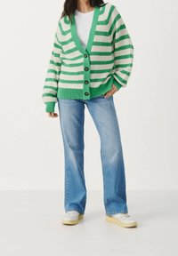 Cardigan a strisce verde e bianche con scollatura a V, texture a coste e cinque bottoni. Abbinato a jeans svasati blu chiaro e sneakers bianche.