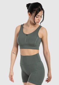 Olivově zelený sportovní set skládající se z úzkého crop topu se zipem vpředu a šortek s vysokým pasem, které mají ozdobné švy a kapsy.