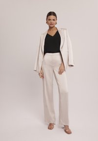 Beżowa satynowa marynarka połączona z czarną bluzką z dekoltem w szpic i beżowymi spodniami. Posiada szerokie nogawki i gładką teksturę. Przezroczyste obcasy i wyraziste kolczyki.