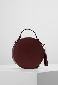 Rund burgunderfarvet læder crossover taske med struktureret overflade, sort rem, lynlåslukning og frynse-accent. Velegnet til forskellige anledninger.