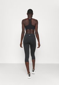 Black sports bra with red accents, black ankle-length leggings, and white athletic shoes. Smooth fabric with fitted design.