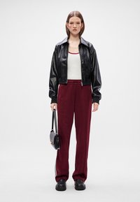 Μαύρο δερμάτινο κοντό μπουφάν, λευκό μπλουζάκι χωρίς μανίκια, μπορντώ παντελόνια φόρμας με κορδόνι και μαύρη τσάντα. Το μοντέλο φοράει ογκώδη μαύρα παπούτσια.