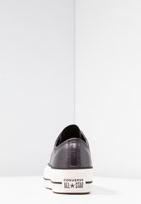 Svarta Converse All Star-skor har ett glänsande ovandelmaterial, rund tå och en tjock vit sula med ett svart rand och logotyp.