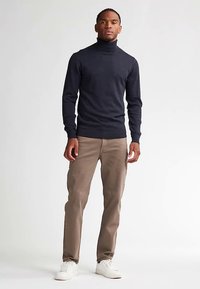 Dunkler Rollkragenpullover, körperbetont, lange Ärmel, kombiniert mit hellbrauner Hose und weißen Sneakern. Glatte Textur, minimalistisches Design.