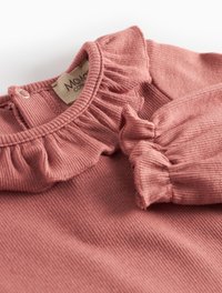 Rosa gerippter Oberteil mit einem Rüschenkragen und puffigen Ärmeln. Mit einem Knopfverschluss auf der Rückseite und einem Etikett mit dem Markennamen.