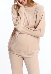 Lichtbeige loungewear-set van zachte stof. Het topje heeft lange mouwen en een ronde halslijn, terwijl de broek aansluitend is met een gladde textuur.