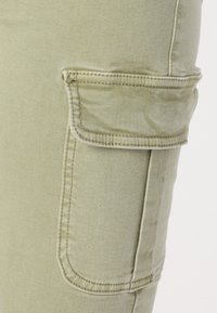 Lichtgroene cargobroek met een zijzak, contrasterende stiksels en een soepele dennenstof. De pasvorm is slank met gestructureerde naden.