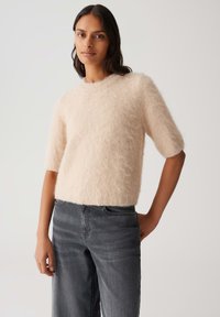 Pudrig rosa, flauschiger Kurzarmpullover mit Rundhalsausschnitt, kombiniert mit dunkelgrauen, weit geschnittenen Jeans aus einem weichen, strukturierten Stoff.