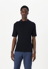 Marinblå kortärmad polo med en texturerad flätstickning, försedda med krage och treknappars knäppning. Matchad med blå byxor.