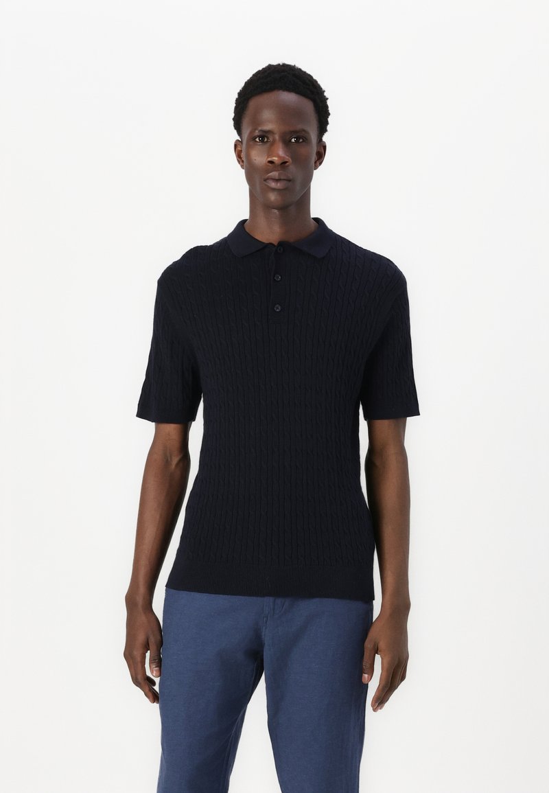 Marinblå kortärmad polo med en texturerad flätstickning, försedda med krage och treknappars knäppning. Matchad med blå byxor.