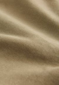 Bēša audums ar smalkām paralēlām līnijām. Mīksts, elastīgs materiāls ar gludu virsmu, kas gaismā parāda smalku spīdumu.