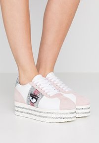 Vita och rosa plattformssneakers med glittrande detaljer, med en ögondesign på sidan och en texturerad mockaöverdela. Klassisk snörning.