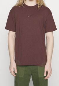 Burgundská bavlněná tričko s krátkým rukávem, kulatým výstřihem a vyšitým logem Nike na hrudi; spárováno se zelenými cargo kalhotami.