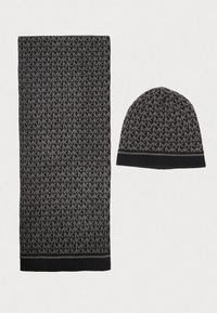 Écharpe tricotée noire et grise avec logo "MK" en motif, assortie d'un bonnet au toucher doux avec un revers côtelé. Les deux articles présentent une texture douce.