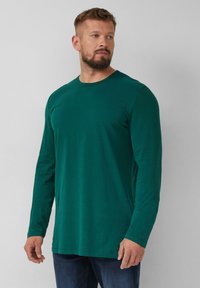 Groen langärmig shirt van zachte katoen, met een ronde halslijn en een ontspannen pasvorm, gecombineerd met donkerblauwe jeans.