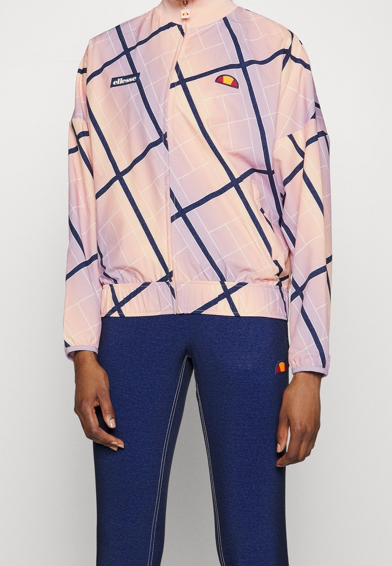 Personne portant une veste à carreaux rose et marine ainsi que des leggings marines, tous deux avec de petits logos de marque colorés sur la poitrine et la cuisse.