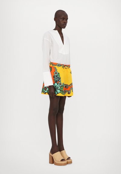 White striped blouse with a V-neck, paired with a colorful yellow skirt featuring floral patterns and a drawstring. Beige heeled clogs.