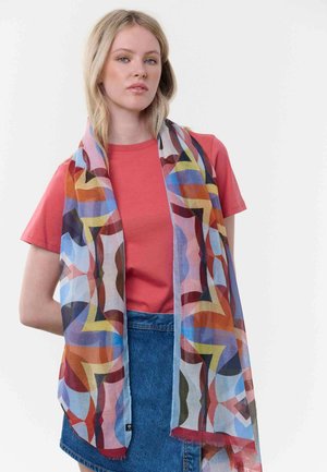 Young woman wearing a coral t-shirt and denim skirt with a colorful geometric patterned scarf draped over her shoulders.