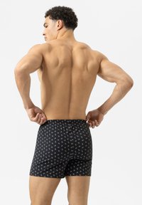 Černé vzorované boxerky s těsným elastickým pasem, které mají malé bílé kruhové vzory a přiléhavý střih.