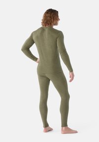 Olivgrön thermoset bestående av en åtsittande långärmad topp och leggings; tillverkad av mjukt, stretchigt material med en texturerad yta.