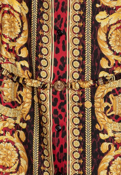 Camisa de tela con un patrón rojo y negro que presenta motivos florales y de animales en dorado, botones negros y un cinturón con acento dorado y un cierre circular.