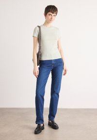 Ljusgrön åtsittande t-shirt, blå raka jeans, svarta loafers. Accessoar: brun axelväska med justerbar rem. Enkelt design, inga mönster.