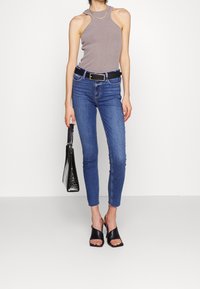 Harmaa ribbikuosinen toppi, jossa olkapäiden leikkausaukot, yhdistetty istuviin sinisiin farkkuihin ja mustiin avoimilla varpailla oleviin mules-kenkiin. Asusteena musta käsilaukku.