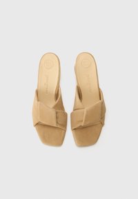 Sandale din suede bej cu un design frontal legat, vârf pătrat și branț căptușit etichetat "SUPER MOALE". Talpă plată pentru confort.