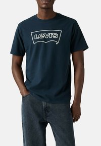 T-shirt en coton bleu marine avec un logo Levi's blanc sur la poitrine, col rond et manches courtes, associé à un jean foncé.
