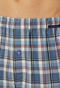 Boxer blu a quadri con un tessuto morbido, caratterizzati da strisce bianche e arancioni, una vita elastica e un'accenno blu in fondo.