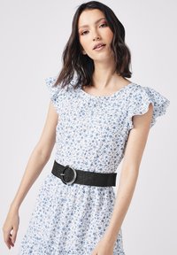Hvid blomsterkjole med blå blomster, flæse ærmer og et sort vævet bælte med en rund spænde. Blød stofstruktur, afslappet pasform.