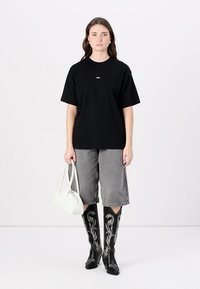 Black oversized T-shirt with a white logo, paired with gray loose shorts, black embroidered knee-high boots, and a white handbag.
