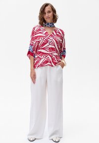 Multicolore, blouse met korte mouwen met een rood tropisch bladpatroon, gecombineerd met losse witte broek en gestreepte schoenen.