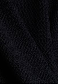 Gros plan sur un tissu tricoté sombre et texturé montrant un motif de maille serré à petite échelle avec de subtils plis et ombres.