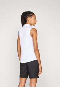 Hvitt ermeløst piké med krage, kombinert med svarte shorts. Glatt stoff, figurnær design og enkle detaljer.