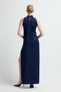 Tmavě modré saténové maxi šaty s vysokým límcem, otevřenými zády a dlouhým zavazovacím detailem; mají boční rozparek a elegantní, přiléhavý střih.