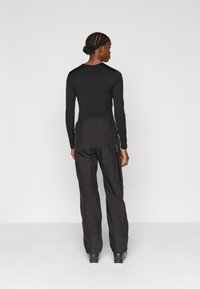 Μαύρο τοπ με μακρύ μανίκι και στρογγυλή λαιμόκοψη, συνδυασμένο με σκούρες παντελόνες που διαθέτουν πλαϊνές τσέπες, ρυθμιζόμενη μέση και ενισχυμένους καρπούς.