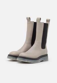 Stivali alla caviglia in pelle beige con pannelli laterali elastici neri, dotati di una suola in gomma spessa e linguette per una facile calzata.