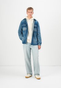 Denim jope, mille peal on hele kapuuts, kergete siniste teksade ja beežide tennistega. Omab kahte rinna taskut ja vabalt voolavat lõiget.