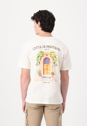 Kremfarget bomull T-skjorte med et akvarellillustrasjon av en dør med blomsterpotter og teksten "Città di Positano" over.
