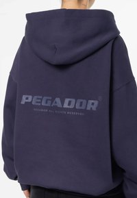 Felpa con cappuccio blu navy realizzata in un tessuto morbido, con un grande logo stampato sul retro e maniche ampie e comode.