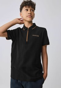 Sort polo-shirt med et struktureret mønster, der har en orange lynlås og kravekant. "BAKER" er broderet i orange på brystet.