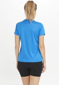 Kortærmet atletisk skjorte i livlig blå farve, med glat tekstur og tætsiddende pasform, parret med sorte shorts. Bagvyn viser et minimalistisk design.