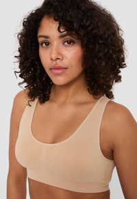 Reggiseno sportivo beige con un design senza cuciture, spalline larghe e fascia testurizzata. Realizzato in materiale morbido, offre una vestibilità comoda.