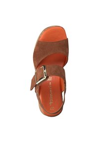 Sandale en daim marron avec deux brides croisées et une boucle dorée. Semelle intérieure orange et semelle extérieure texturée. Design à bout ouvert.