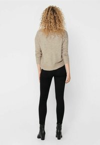 Beżowy sweter o luźnym kroju, z prążkowanymi mankietami i zaokrąglonym dołem, w połączeniu z czarnymi rurkami i botkami za kostkę. Widok z tyłu na strój.