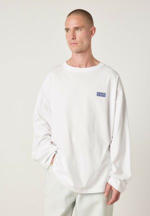 Hvid langærmet t-shirt i blød bomuld med rund halsudskæring, afslappet pasform og lille blå "American Vintage"-logo på brystet.