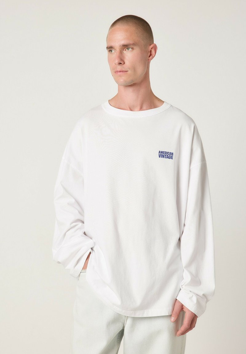 Valge pikkade varrukatega T-särk pehmest puuvillast, millel on ümar kaelus, lõõgastunud lõige ning väike sinine "American Vintage" logo rinnal.