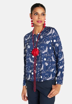 Navy long-sleeve top featuring white cranes and floral patterns, with round neckline and red bead necklace with a fabric flower accent.